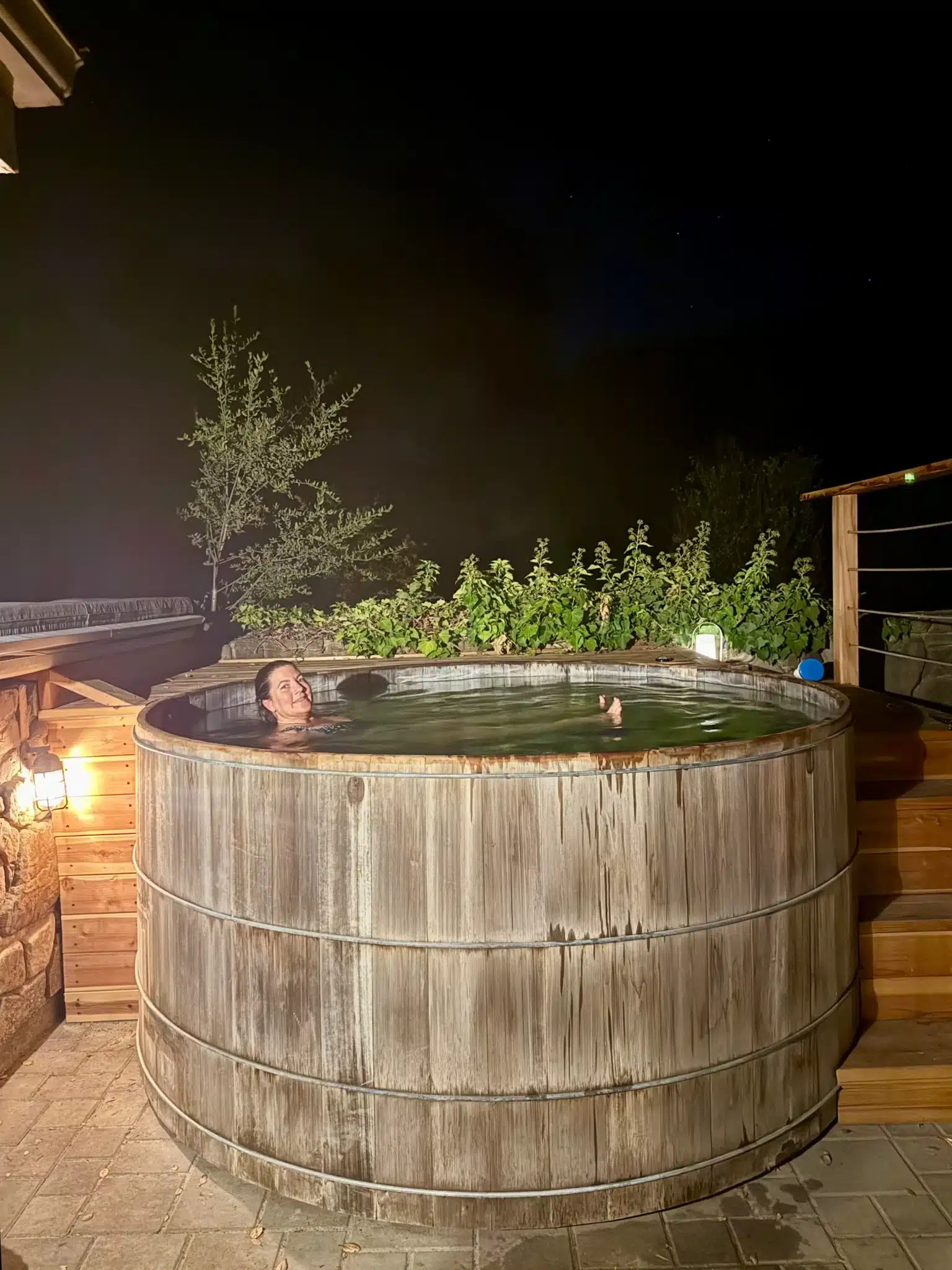 Rustic wooden hot tub steaming at night on a patio with lantern light and greenery, a local produce stall near Ojai grocery